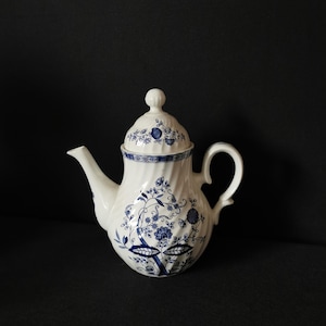 Pode incluir: Uma chaleira branca com um desenho floral azul e branco. A chaleira tem uma tampa e uma alça.