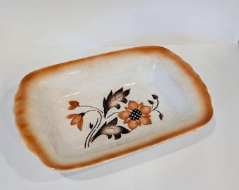 May include: A white ceramic baking dish with a brown rim and a floral design in shades of brown and orange.