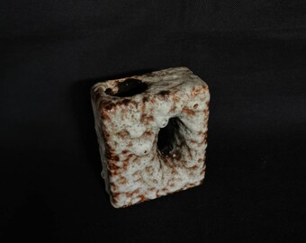 May include: A white and brown ceramic vase with a rough, textured surface. The vase has a rectangular shape with a cutout on one side.
