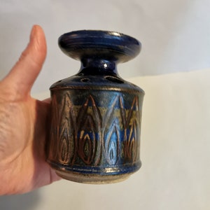Könnte beinhalten: Eine kleine, blaue und braune Keramikvase mit einem dekorativen Muster. Die Vase hat einen breiten, flachen Boden und einen schmalen Hals.