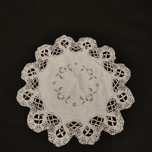 Può includere: Tovaglietta all'uncinetto bianca con un delicato disegno floreale al centro.
