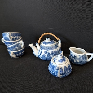 Puede incluir: Un juego de té de porcelana azul y blanco con una tetera, una jarra de crema, un azucarero y cuatro tazas. La tetera tiene un asa de bambú y el juego presenta un diseño chino tradicional.