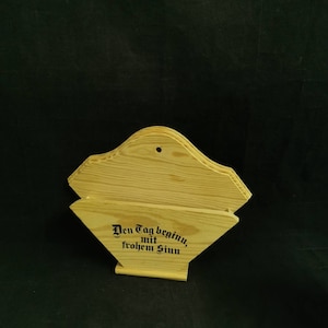 Könnte beinhalten: Holz-Kaffeefilterhalter mit dem Text "Den Tag beginn, mit frohem Sinn" in schwarzer Schrift.