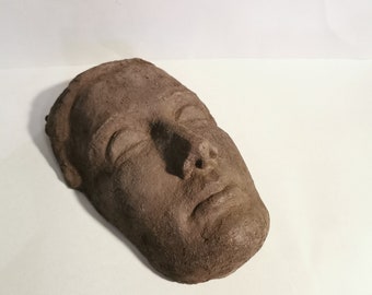 Könnte beinhalten: Eine braune Tonskulptur eines Gesichts mit geschlossenen Augen und leicht geöffnetem Mund.