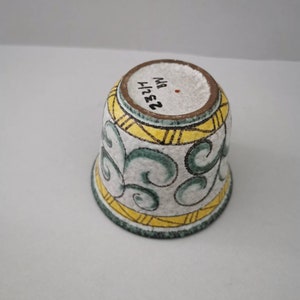 Könnte beinhalten: Weiße Keramiktasse mit grünem und gelbem Design. Der Boden der Tasse trägt die Nummer "2324" und die Buchstaben "M.B." in Schwarz.