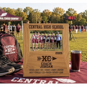 May include: A light-colored wooden picture frame featuring the text CENTRAL HIGH SCHOOL at the top, the year 2026, an arrow graphic with XC, the words COACH JORDAN, and a list of names including Hayden, Beau, Neil, Corbin, Sammy, Greyson, Jordy, Kanaloa, Leo, Mason, Nathan, and Adam.