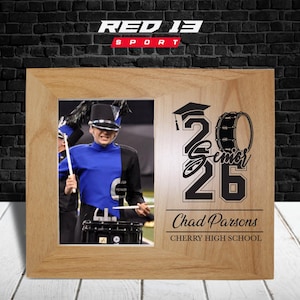 May include: Wooden picture frame with a photo of a marching band member in a blue uniform. The frame is engraved with "Senior 26", a graduation cap, a drum, the name "Chad Parsons", and "Cherry High School". The Red 13 Sport logo is at the top.