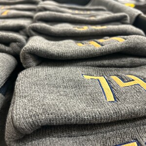 May include: A stack of gray knit beanies with a yellow embroidered number "74" on the top beanie.