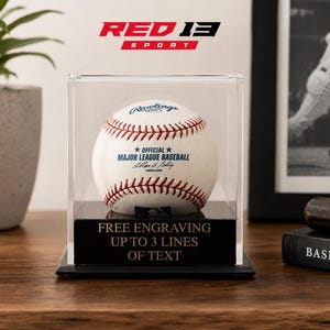 May include: A Major League Baseball in a clear display case. The baseball is white with red stitching and the Rawlings logo. The display case has a black base with the text "FREE ENGRAVING UP TO 3 LINES OF TEXT". The Red 13 Sport logo is at the top.