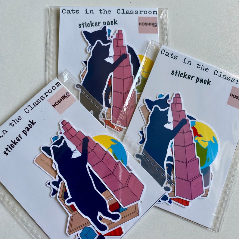 May include: Three sticker packs featuring illustrations of cats in a classroom setting. Each pack has the text "Cats in the Classroom sticker pack" and the brand name "HOSHIKS". The stickers feature cats interacting with classroom objects like a globe, a stack of blocks, and a bookshelf.