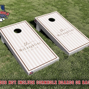 Könnte beinhalten: Zwei rechteckige Cornhole-Boards mit einem hellbeigen und weißen vertikalen Streifenmuster und einem braunen Rand. Jedes Board hat ein kreisförmiges Loch an der Oberseite und ist mit dem Text "the McLaughlins" und dem Datum "07 24 26" versehen.