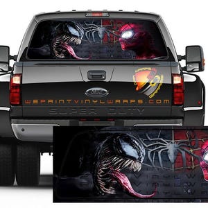 Puede incluir: Camión negro con un gráfico de Venom y Spider-Man enfrentados en la ventana trasera. El gráfico está impreso en una pegatina de vinilo transparente. El camión tiene un emblema "Super Duty" en el portón trasero.