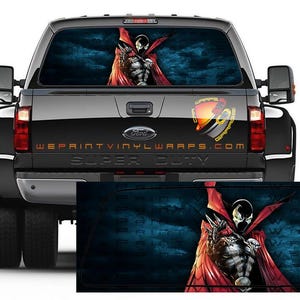 Könnte beinhalten: Ein schwarzer Ford Super Duty-Truck mit einer Heckscheibengrafik, die eine Comicfigur mit rotem Umhang vor blauem Hintergrund zeigt. Der Text "WEPRINTVINYLWRAPS.COM" ist sichtbar.