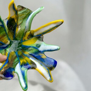 Puede incluir: Un cuenco de vidrio abstracto y colorido con un dise&ntilde;o de estrella. El cuenco presenta tonos vibrantes de amarillo, azul, verde y blanco. El cuenco &uacute;nico, hecho a mano, es una pieza decorativa.