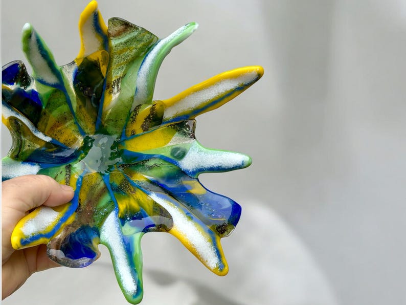 Puede incluir: Un cuenco de vidrio abstracto y colorido con un dise&ntilde;o de estrella. El cuenco presenta tonos vibrantes de amarillo, azul, verde y blanco. El cuenco &uacute;nico, hecho a mano, es una pieza decorativa.