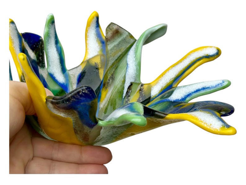 Puede incluir: Escultura abstracta de vidrio con colores vibrantes. La pieza presenta tonos de amarillo, azul, verde y blanco, creando un dise&ntilde;o din&aacute;mico. La forma de la escultura recuerda a una flor floreciendo o una explosi&oacute;n de energ&iacute;a. Medidas en cent&iacute;metros.