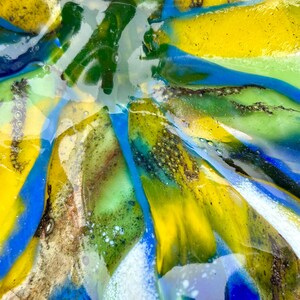 Puede incluir: Primer plano de un cuenco de vidrio colorido con un dise&ntilde;o abstracto &uacute;nico. El cuenco presenta tonos vibrantes de amarillo, azul, verde y blanco, creando un efecto visual llamativo. El vidrio parece texturizado y en capas, agregando profundidad al dise&ntilde;o.