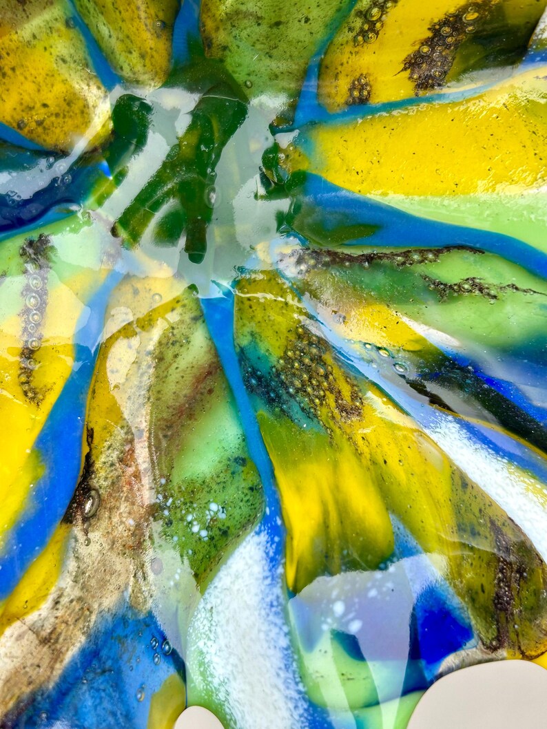 Puede incluir: Primer plano de un cuenco de vidrio colorido con un dise&ntilde;o abstracto &uacute;nico. El cuenco presenta tonos vibrantes de amarillo, azul, verde y blanco, creando un efecto visual llamativo. El vidrio parece texturizado y en capas, agregando profundidad al dise&ntilde;o.