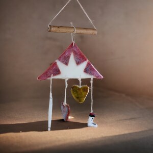 May include: A handmade wind chime featuring a red and white triangular top with a star design. Below hang a yellow heart, a red heart, and a small white boot with black accents. The chime is suspended from a wooden dowel.