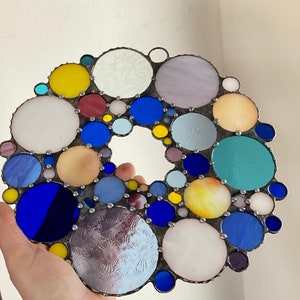 May include: A stained glass suncatcher with a circular design featuring various colors and sizes of glass circles. The colors include blue, yellow, red, white, and purple.