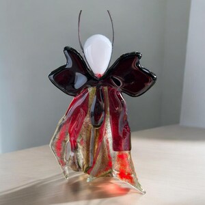 Könnte beinhalten: Eine Glasskulptur eines stilisierten Schmetterlings in Rot-, Gold- und Schwarztönen. Der Schmetterling hat eine weiße Mitte und eine schwarze Schleife.