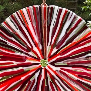 May include: A round, red, white, and gold glass suncatcher with a radial design. The suncatcher is made of multiple layers of glass, creating a layered effect.