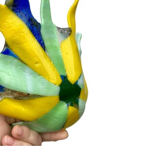 Puede incluir: Una colorida pieza de arte en vidrio con un dise&ntilde;o abstracto &uacute;nico. La pieza presenta colores vibrantes amarillo, azul, verde y blanco. El vidrio tiene forma org&aacute;nica, con una superficie texturizada. La pieza se sostiene en una mano.