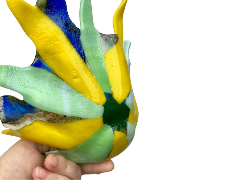 Puede incluir: Una colorida pieza de arte en vidrio con un dise&ntilde;o abstracto &uacute;nico. La pieza presenta colores vibrantes amarillo, azul, verde y blanco. El vidrio tiene forma org&aacute;nica, con una superficie texturizada. La pieza se sostiene en una mano.