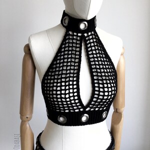 May include: Black crochet halter top with a high collar and a keyhole design. The top features silver grommets around the collar and the bottom hem. The top is displayed on a mannequin.