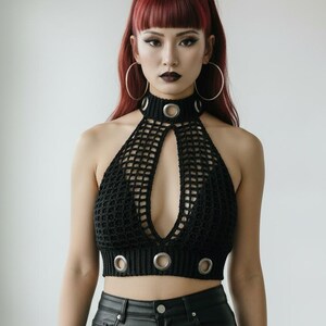 May include: Black halter top with a keyhole design and metal ring accents. The top is made of a crocheted material. The model is wearing black leather pants and large hoop earrings.