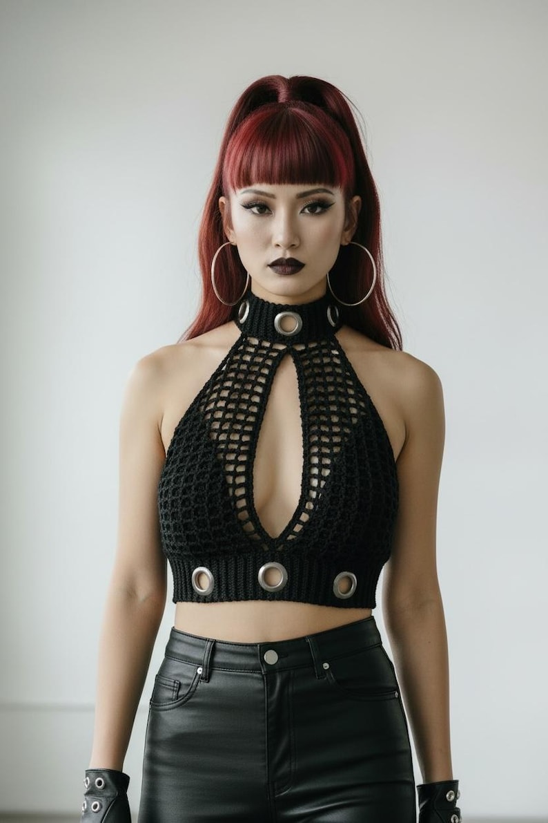 May include: Black halter top with a keyhole design and metal ring accents. The top is made of a crocheted material. The model is wearing black leather pants and large hoop earrings.