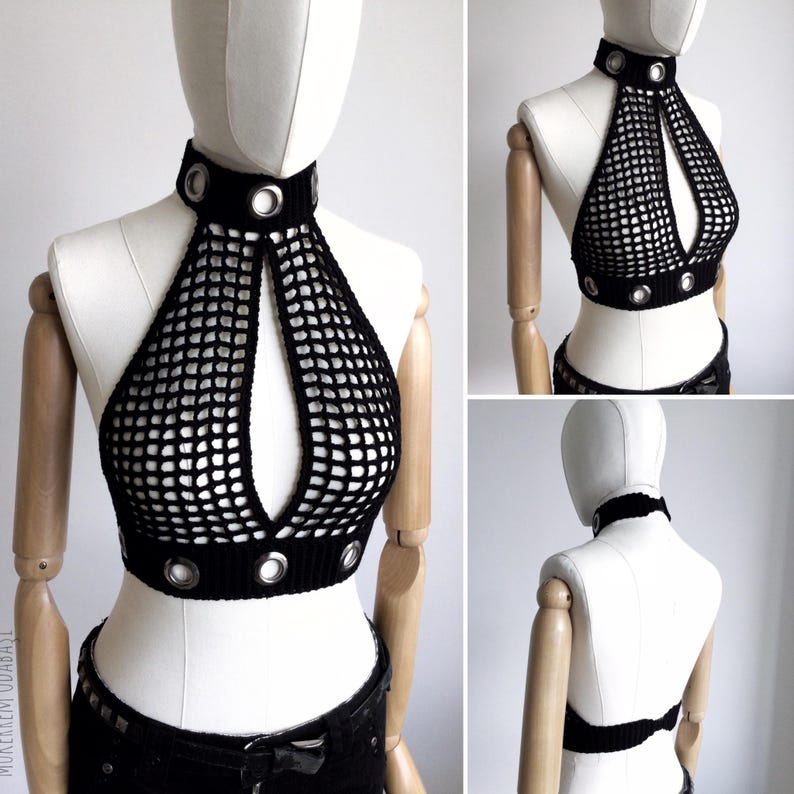 May include: Black crochet halter top with a high collar and a keyhole design. The top features silver grommets around the collar and the bottom hem. The open weave creates a net-like appearance. The top is displayed on a mannequin.