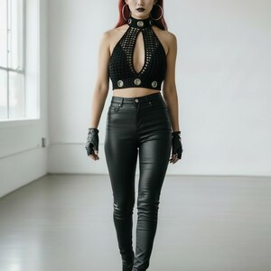 May include: Black halter top with a keyhole design and silver accents. The top is paired with black leather pants and boots. The model is wearing black fingerless gloves and large hoop earrings. The background is a white studio.