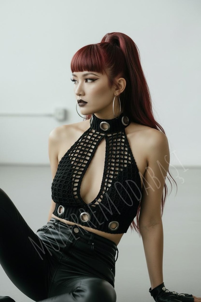 May include: Black crochet halter top with a keyhole neckline and silver grommet details. The top is part of a fashion ensemble. The model has red hair and is wearing large hoop earrings.