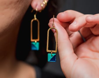 Peut inclure: Boucles d'oreilles géométriques dorées avec des accents géométriques bleus et verts. Les boucles d'oreilles pendent du lobe de l'oreille.