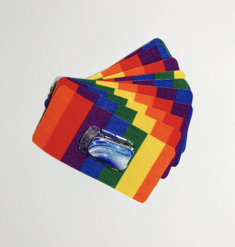 Peut inclure: Un empilement de patchs en tissu aux couleurs de l'arc-en-ciel avec un petit autocollant transparent bleu et blanc sur le patch du dessus.