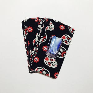 Peut inclure: Une pile de tissu noir avec un motif de cr&acirc;ne blanc et de fleurs rouges. Un comprim&eacute; de savon bleu et blanc est pos&eacute; sur le tissu.