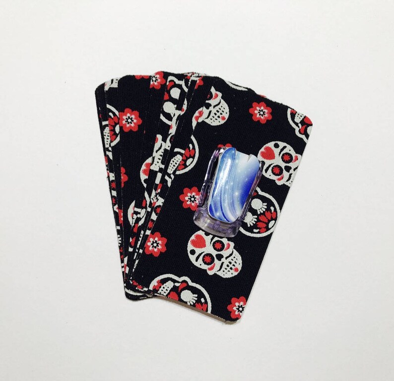 Peut inclure: Une pile de tissu noir avec un motif de cr&acirc;ne blanc et de fleurs rouges. Un comprim&eacute; de savon bleu et blanc est pos&eacute; sur le tissu.