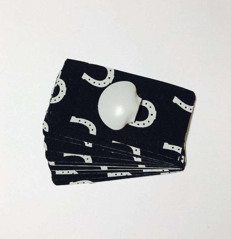 Op de afbeelding: Een stapel zwarte stofvierkanten met witte hoefijzerpatronen. Een witte plastic knop is bevestigd aan het bovenste vierkant.