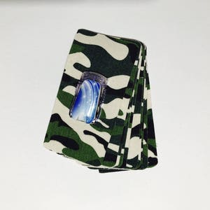 Peut inclure: Une pile de tissu camouflage avec un flacon de vernis &agrave; ongles bleu et blanc sur le dessus.