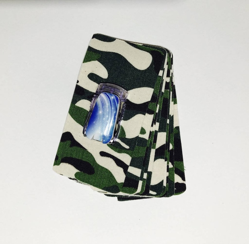 Peut inclure: Une pile de tissu camouflage avec un flacon de vernis &agrave; ongles bleu et blanc sur le dessus.