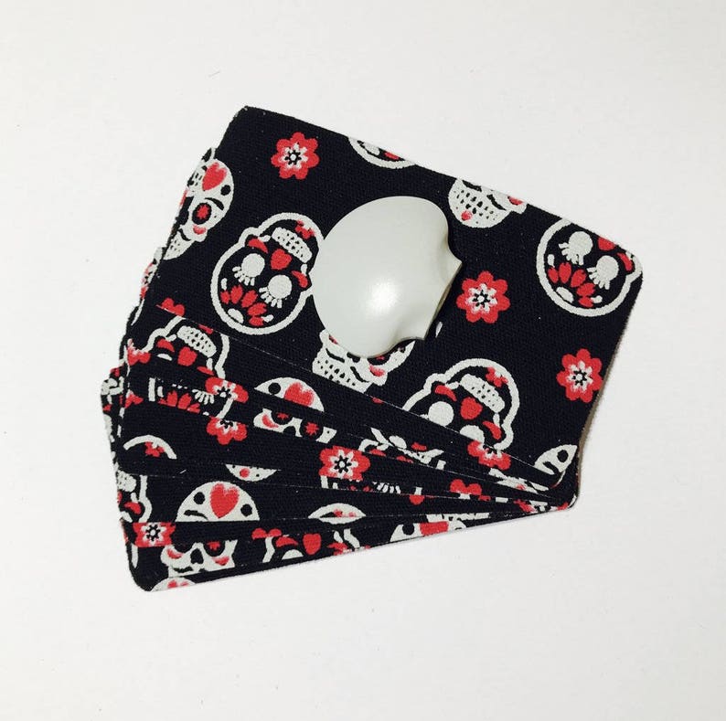 Op de afbeelding: Een stapel zwarte stoffen kaarten met een patroon van witte schedels en rode bloemen. De kaarten zijn dubbelgevouwen en hebben een witte plastic knop aan de bovenkant.