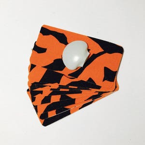 Op de afbeelding: Een stapel oranje en zwarte stoffen kaarten met een witte knop erop.