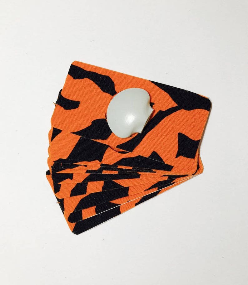 Op de afbeelding: Een stapel oranje en zwarte stoffen kaarten met een witte knop erop.