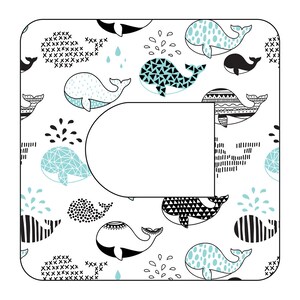 Può includere: Uno sfondo bianco con un motivo ripetuto di balene nere e blu. Le balene sono in vari stili, tra cui geometrico, a pois e a righe. Lo sfondo include anche piccole gocce di pioggia nere.