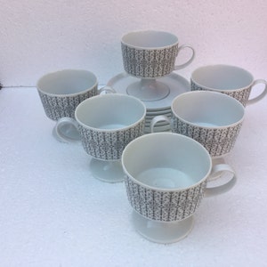 May include: Set of six white ceramic coffee cups with black geometric patterns. Each cup has a pedestal base and a handle.