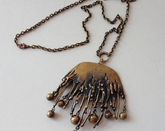 May include: A gold-toned necklace with a large, abstract pendant featuring a textured, dripping design and small round beads.