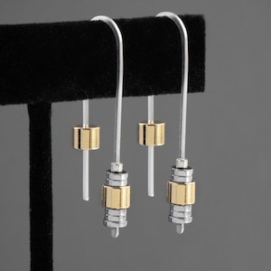 May include: Silver and gold-tone metal earrings with a linear design. The earrings have a long, curved hook and feature cylindrical gold and silver accents. The text "SAMPLE OF MIXED METAL 1.5 LENTH" is visible.