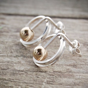 May include: A pair of silver hoop earrings with a gold ball accent. The earrings are simple and elegant, and would make a great gift for any occasion.