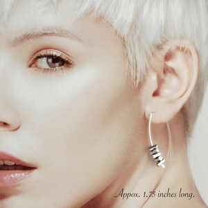 May include: Silver-toned earrings with a curved design, featuring a cluster of small, dark gray geometric beads. The earrings are approximately 1.75 inches long.